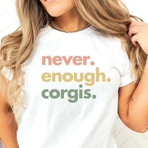 May include: A white t-shirt with the text "never. enough. corgis." printed in pink, yellow, and green.
