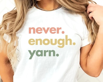 May include: White t-shirt with the text "never. enough. yarn." in colorful lettering.
