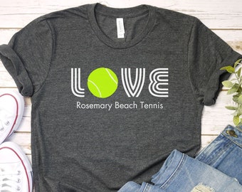 May include: A dark gray t-shirt with the word "LOVE" in white with a tennis ball in the "O". The text "Rosemary Beach Tennis" is below the word "LOVE".