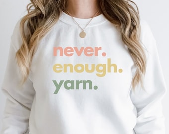May include: White sweatshirt with the text "never. enough. yarn." in pastel colors.