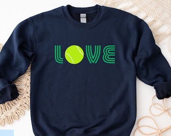 May include: Navy blue sweatshirt with the word "LOVE" in green outlined letters. A green and yellow tennis ball is in the center of the word "LOVE".