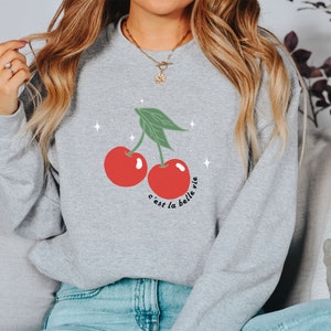 May include: A gray sweatshirt with a graphic of two red cherries and the text "c'est la belle vie".