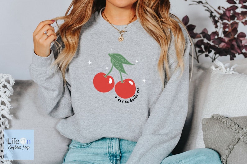 May include: A gray sweatshirt with a graphic of two red cherries and the text "c'est la belle vie".
