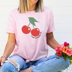May include: Pink t-shirt with a graphic of two red cherries and the text "c'est la belle vie".