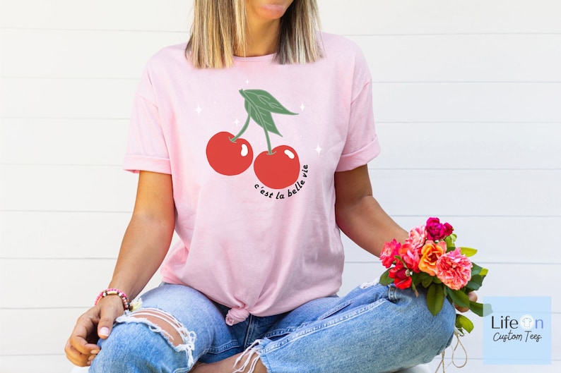 May include: Pink t-shirt with a graphic of two red cherries and the text "c'est la belle vie".