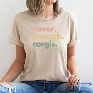 May include: A beige t-shirt with the text "never. enough. corgis." printed in a rainbow color scheme.