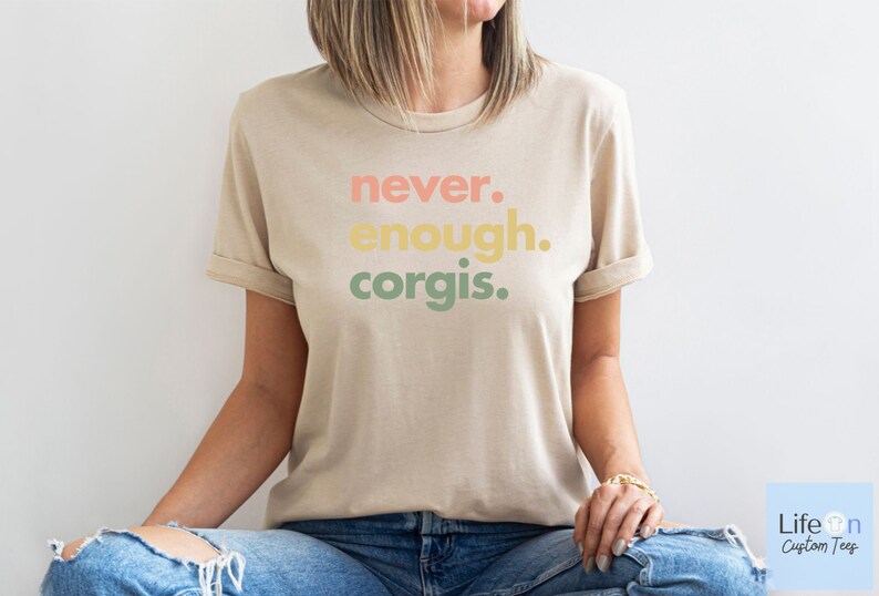 May include: A beige t-shirt with the text "never. enough. corgis." printed in a rainbow color scheme.