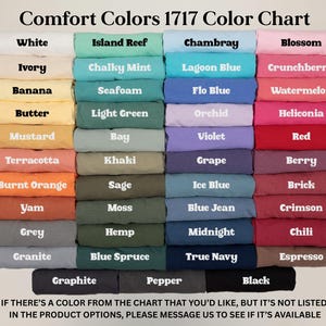 Puede incluir: Una carta de colores Comfort Colors 1717 que muestra muestras de tela dobladas en varios tonos. Los colores incluyen blanco, azul, rosa y verde. El texto en la parte inferior anima a los clientes a preguntar por colores no listados.