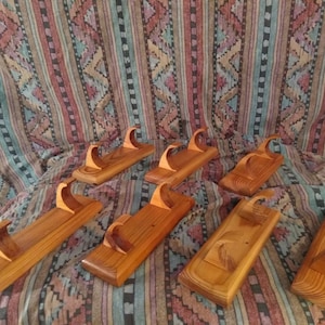 Puede incluir: Varios expositores de madera hechos a mano con una parte superior curvada y una base rectangular están dispuestos sobre una tela estampada. Los expositores están hechos de madera marrón clara y oscura, mostrando la veta natural.