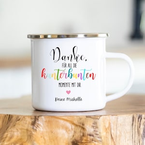 Puede incluir: Taza de esmalte blanco con borde y asa plateados. La taza presenta el texto "Danke, für all die kunterbunten Momente mit dir. Deine Michelle" en letras negras y coloridas, con un corazón rosa.