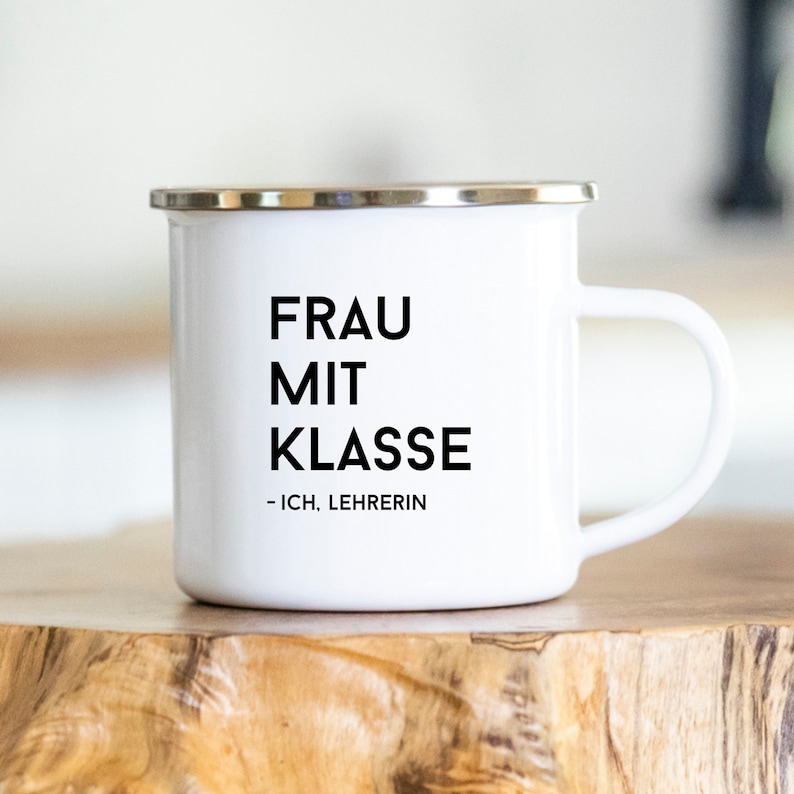 May include: White enamel mug with black text that reads "Frau mit Klasse - Ich, Lehrerin".
