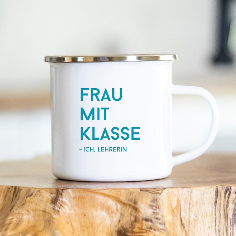May include: White enamel mug with a blue inscription that reads "FRAU MIT KLASSE - ICH. LEHRERIN".