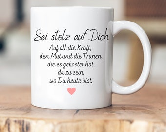 Puede incluir: Taza de cerámica blanca con una inscripción en negro que dice "Sei stolz auf Dich. Auf all die Kraft, den Mut und die Tränen, die es gekostet hat, da zu sein, wo Du heute bist." Un pequeño corazón rosa se encuentra en la parte inferior de la inscripción.
