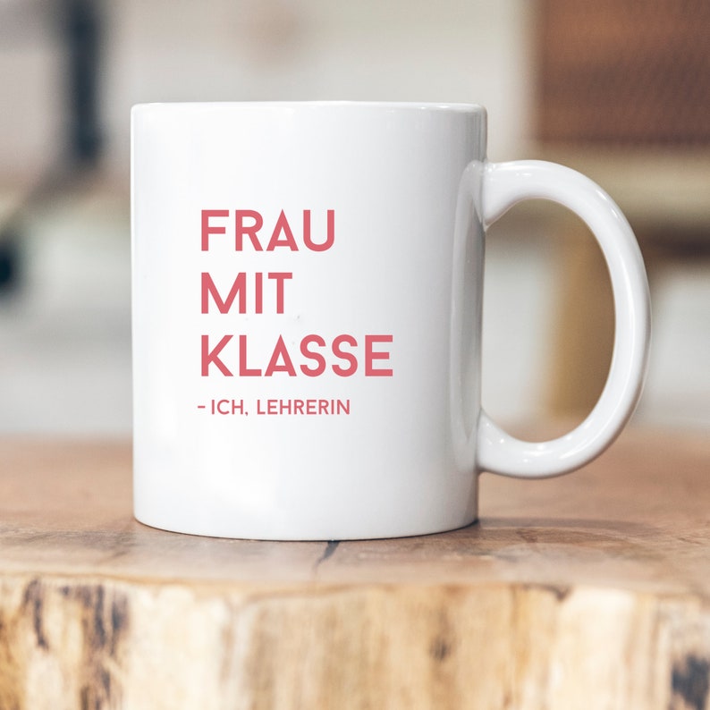 May include: White ceramic mug with the text "FRAU MIT KLASSE - ICH, LEHRERIN" in red.