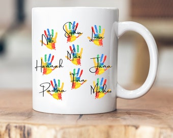 Puede incluir: Taza de cerámica blanca con diseños de huellas de manos coloridas y nombres escritos en cursiva negra. Los nombres son: Niko, Sophia, Louisa, Hannah, Max, Jana, Paulina, Finn y Matheo.