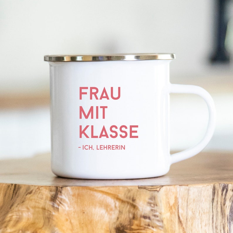 May include: White enamel mug with a silver rim. The mug has the text "FRAU MIT KLASSE - ICH, LEHRERIN" printed in pink.
