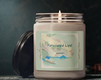 May include: A clear glass candle jar with a black lid and a lit wick. The label features a watercolor illustration of a boat on water with the text "Purposeful Life!" and "Unscented" printed in a dark green font on a light green background.