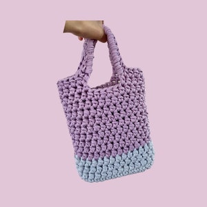 Op de afbeelding: Een gehaakte tote bag in lavendel en lichtblauw met een enkele handvat.