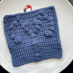 Op de afbeelding: Een blauwe vierkante gehaakte theedoek met een textuurpatroon.