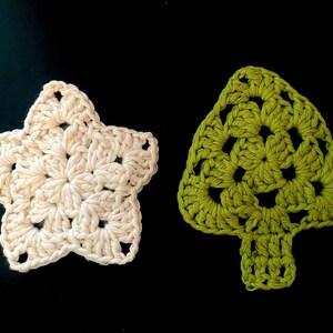 Op de afbeelding: Twee gehaakte ornamenten, een in de vorm van een ster in crème en de andere in de vorm van een kerstboom in groen.