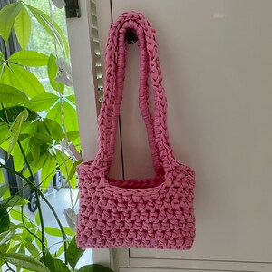 Op de afbeelding: Een roze gehaakte tote bag met een enkele band.
