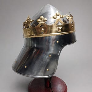 May include: A polished steel helmet featuring a pointed crown and a wide, flared neck guard. A decorative brass band with fleur-de-lis accents and small square studs encircles the base of the crown, secured with small brass rivets to the steel.