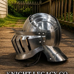 May include: A polished steel knight helmet featuring a rounded dome, a hinged visor with vertical ventilation slits, and a neck guard. The text KNIGHT LEGACY CO. is printed below the helmet, accompanied by a small shield icon and two swords.