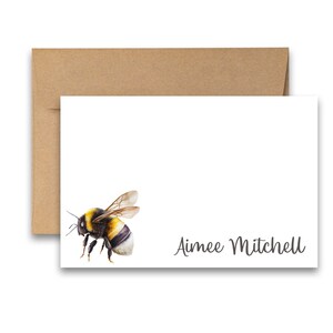 Puede incluir: Una tarjeta blanca con una ilustraci&oacute;n de abejorro negro y amarillo y el texto "Aimee Mitchell" en cursiva negra.