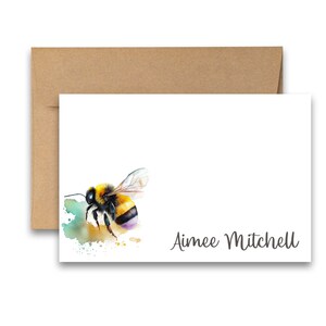 Puede incluir: Una tarjeta blanca con una pintura de acuarela de un abejorro sobre un fondo verde y amarillo. El texto "Aimee Mitchell" est&aacute; impreso en gris en la parte inferior de la tarjeta.