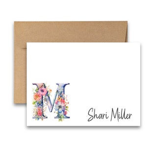 May include: A white card with a blue and pink floral letter M and the text "Shari Miller" in black cursive.