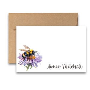 Puede incluir: Una tarjeta blanca con una ilustraci&oacute;n de acuarela de un abejorro en una flor morada. El texto "Aimee Mitchell" est&aacute; impreso en gris en la parte inferior de la tarjeta.