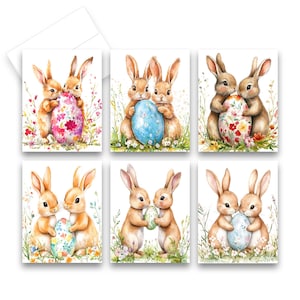 May include: Set of six Easter greeting cards featuring watercolor illustrations of bunnies with decorated eggs. The cards showcase bunnies in various poses, holding or embracing colorful eggs with floral patterns. The cards are on a white background.