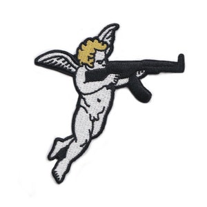 以下が含まれることがあります： 黒いライフルを持っている、金色の髪と黒い翼を持つ白いケルビムが描かれた刺繍パッチ。パッチは黒い縁取りがあり、布にアイロンをかけたり縫い付けたりするように設計されています。