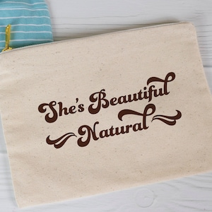 May include: A beige canvas zippered pouch with the text "She's Beautiful Natural" printed in brown cursive font.