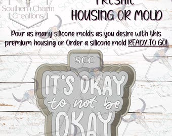 May include: A gray Freshie housing or mold with the text "IT'S OKAY to not be OKAY" in white. The image also includes the text "FRESHIE HOUSING OR MOLD" and "Pour as many silicone molds as you desire with this premium housing or Order a silicone mold READY TO GO!"