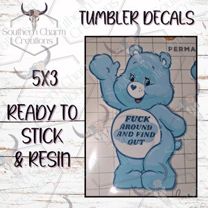 K&ouml;nnte beinhalten: Hellblauer Care Bear-Stil Aufkleber mit dem Text "FUCK AROUND AND FIND OUT" auf dem Bauch. Der Aufkleber ist 12,7 x 7,6 cm gro&szlig; und ist zum Aufkleben und Verharzen bereit. Der Text "Tumbler Decals" steht oben.