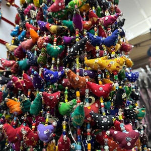 May include: A colourful garland of fabric birds with beaded accents. The birds are in various colours and patterns, including red, green, blue, yellow, and purple. The garland is perfect for adding a touch of whimsy to any space.