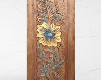 May include: A wooden door with a carved floral design. The flower is yellow with a blue center and is surrounded by green leaves. The door is painted in shades of brown, blue, and green.