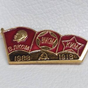 May include: A red, white, and gold enamel pin with three flags. The flags have the text "ВЛКСМ 1988", "ВЛКСМ", and "КЛМ 1918" on them. The pin features a red star and a hammer and sickle.