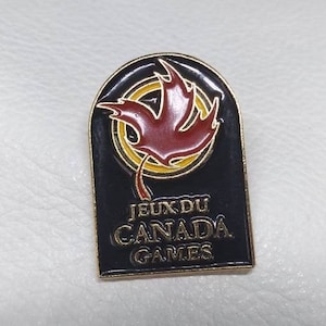 May include: A gold and black pin with a red maple leaf design. The text "Jeux du Canada Games" is printed on the pin.