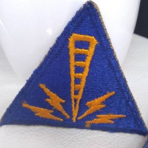 May include: Two blue and gold triangular patches with a lightning bolt and tower design. The patches are made of felt and have a rough texture.