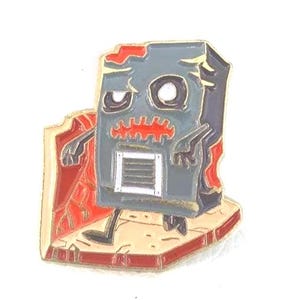 May include: A gray and red enamel pin featuring a cartoon zombie computer. The pin has a distressed look with a red cape and a beige base. The zombie computer has a rectangular body, a vent, and a sad expression.