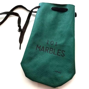 May include: A green leather pouch with the text "101 MARBLES" printed on the front. The pouch has a drawstring closure and a black cord. The word "JAPAN" is printed below the text.