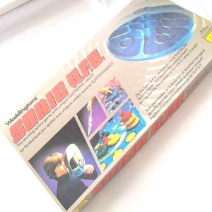 May include: A vintage "Sonic UFO" board game box. The box features a blue plastic UFO toy and game instructions. The box has the text "The exciting space game with unique ELECTRONIC sound!" and "Waddingtons" printed on it.