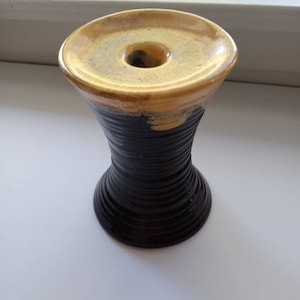 May include: A ceramic vase with a black and yellow glaze. The vase has a wide mouth and a narrow base.