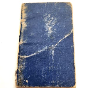 Peut inclure: Un petit carnet rectangulaire vintage avec une couverture en cuir bleu vieilli. La couverture présente des signes d'usure, avec des plis visibles et une surface texturée. Les bords sont légèrement usés, suggérant l'âge et l'utilisation.