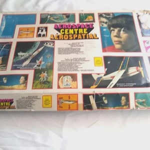 May include: A vintage Aerospace Centre Aerospatial box featuring illustrations of rockets, airplanes, and a young person. The box has a colorful design with the title in large letters. The box is slightly worn.