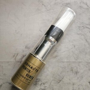 May include: An Ednalite Pointer/Viewer encased in a clear plastic tube. The device features a metallic silver body with a gold-colored base section printed with black text reading EDNALITE POINTER/VIEWER, .014 MINIATURE SCREW-BASE REPLACEMENT BULB, MADE IN USA, PATS PENDING.