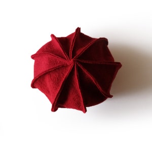 Könnte beinhalten: Eine rote Wollmütze mit einem einzigartigen, segmentierten Design. Die Mütze ist in acht Abschnitte gefaltet, wodurch ein geometrisches Muster entsteht.