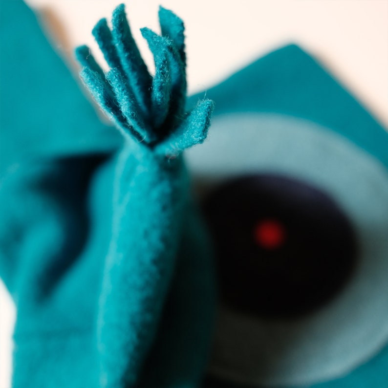 May include: A teal blue felt hat with a fuzzy brim and a small red dot in the centre.